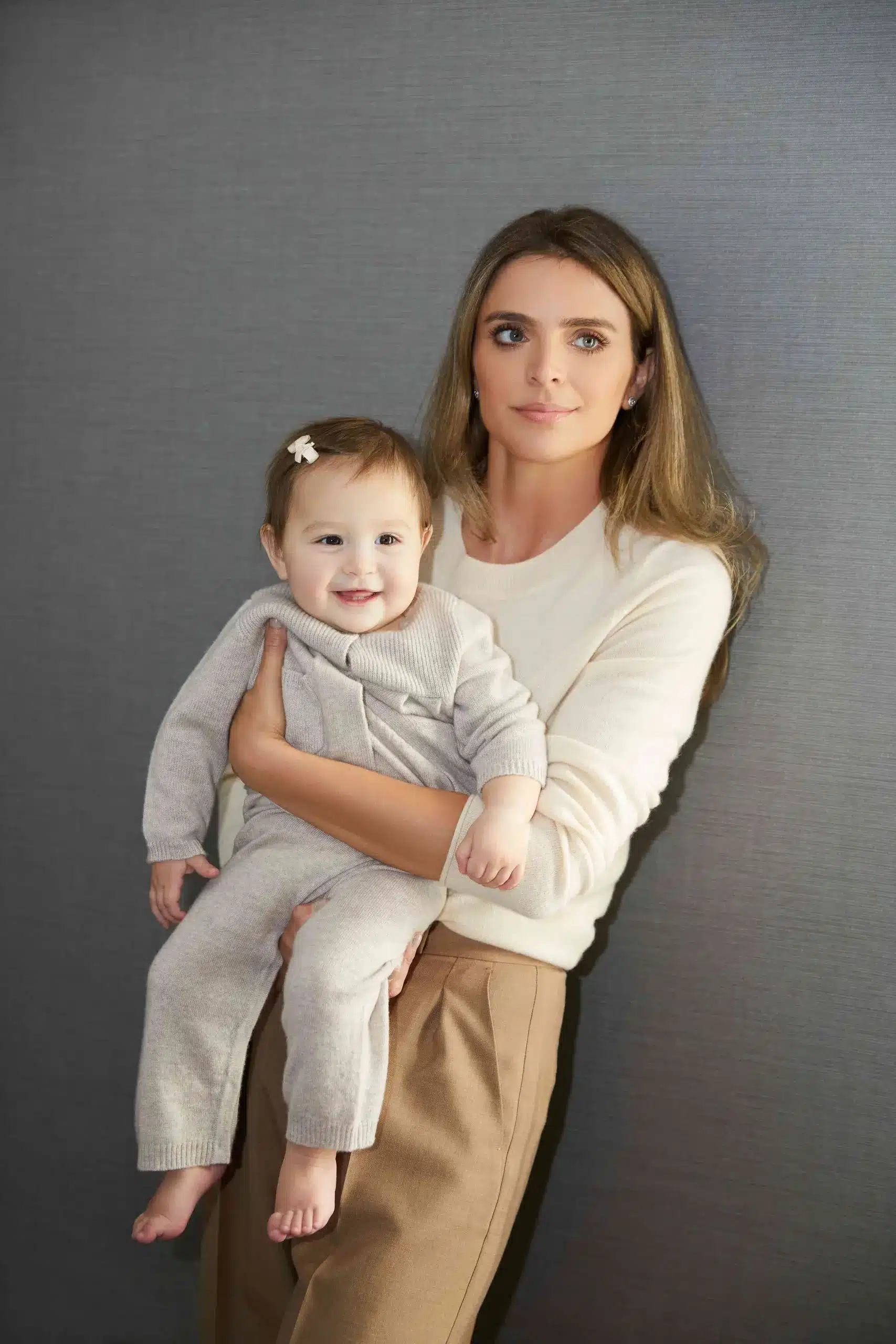 Anna Sweeting, author of "become a CEO in your 20s", stood in a white jumper, holding up her smiling daughter