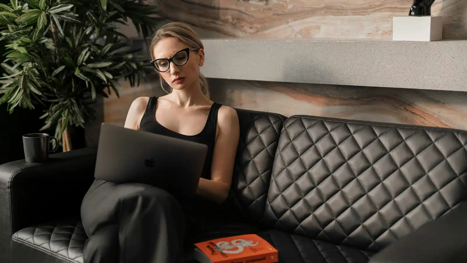 For the "why women feel guilty using AI at work" article, a woman with glasses sat on a brown leather sofa staring at a laptop on her lap